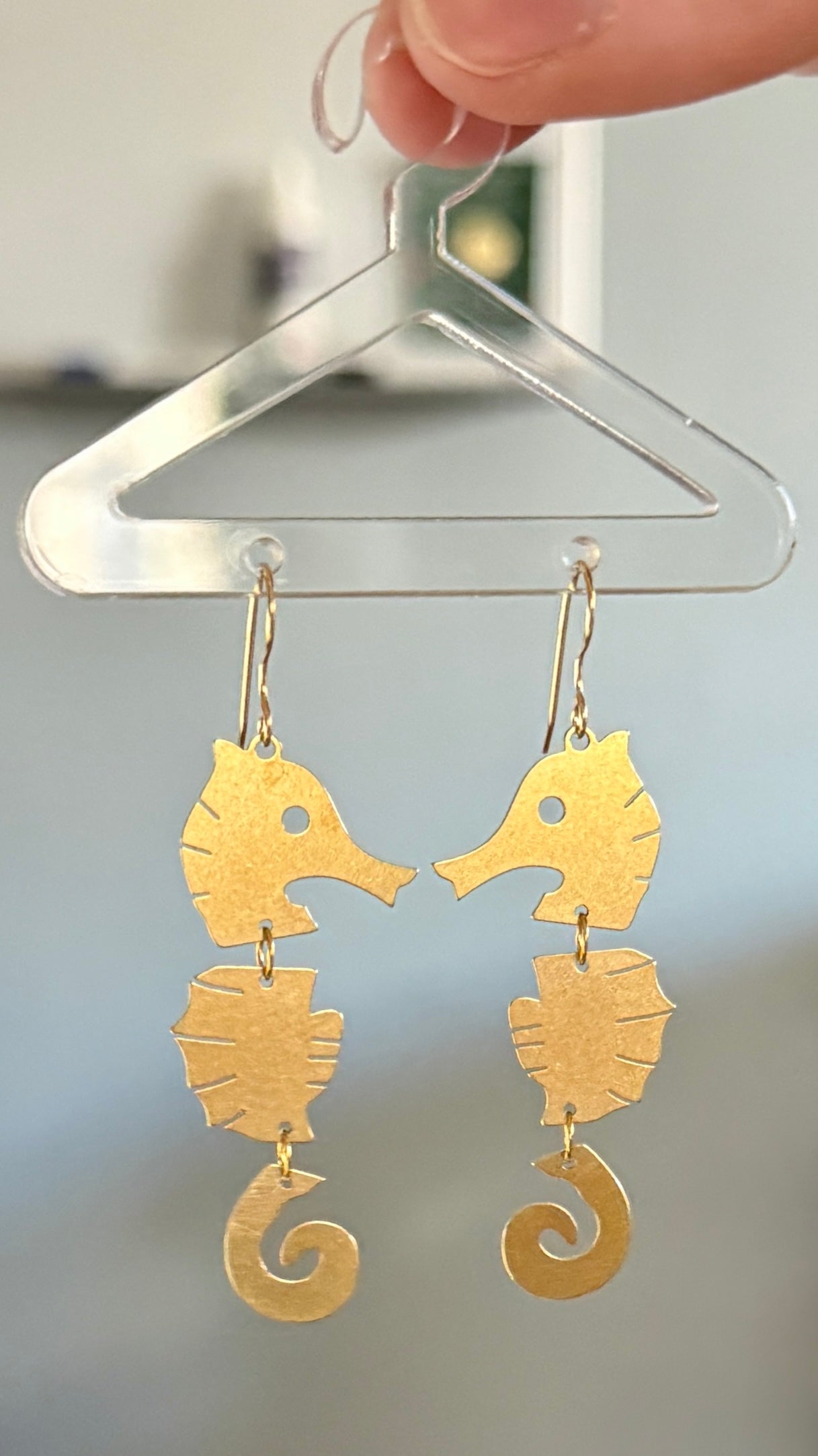 Gold seahorse-shaped earrings hanging on a clear hanger against a neutral background.