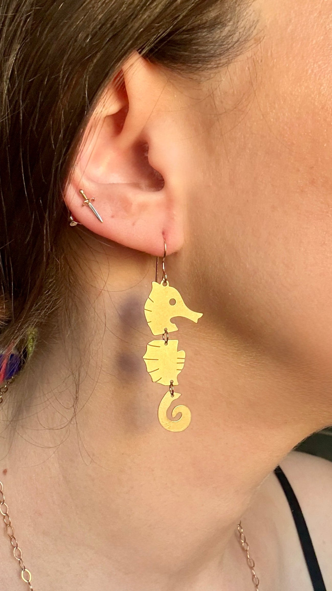 Close-up of a person wearing gold seahorse earrings.