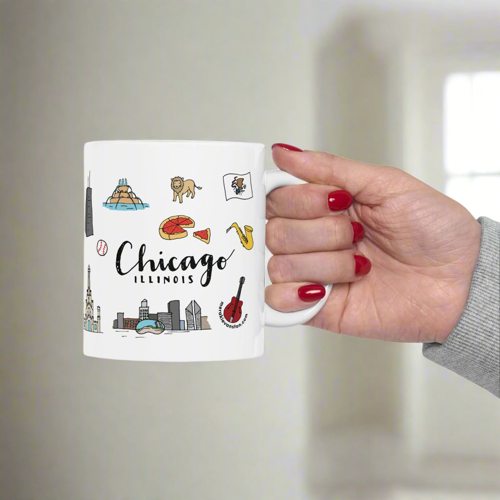 White mug with Chicago-themed illustrations held by a hand on a white background