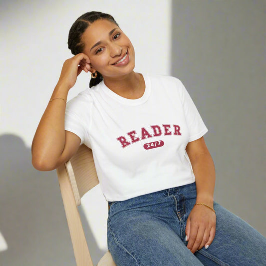 Person wearing a white t-shirt with 'READER 24/7' text, sitting on a chair.