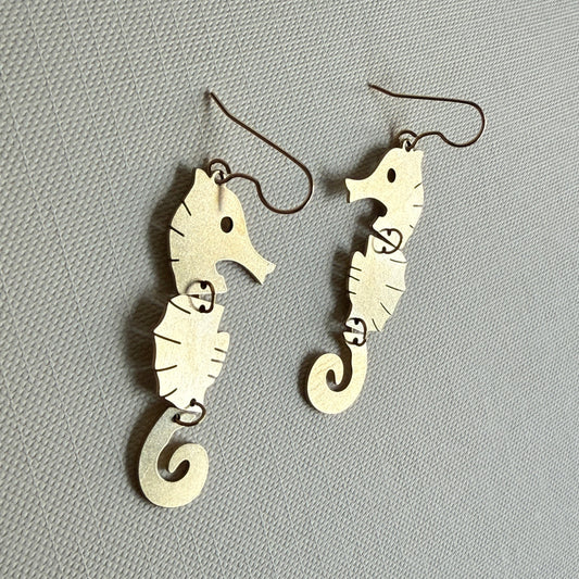 Pair of silver seahorse-shaped earrings on a gray background